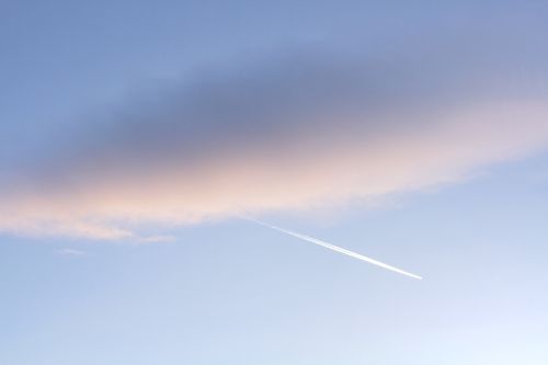 Free A serene sky at dusk with a pastel-colored cloud and a contrail streaking through, creating a peaceful scene. Stock Photo