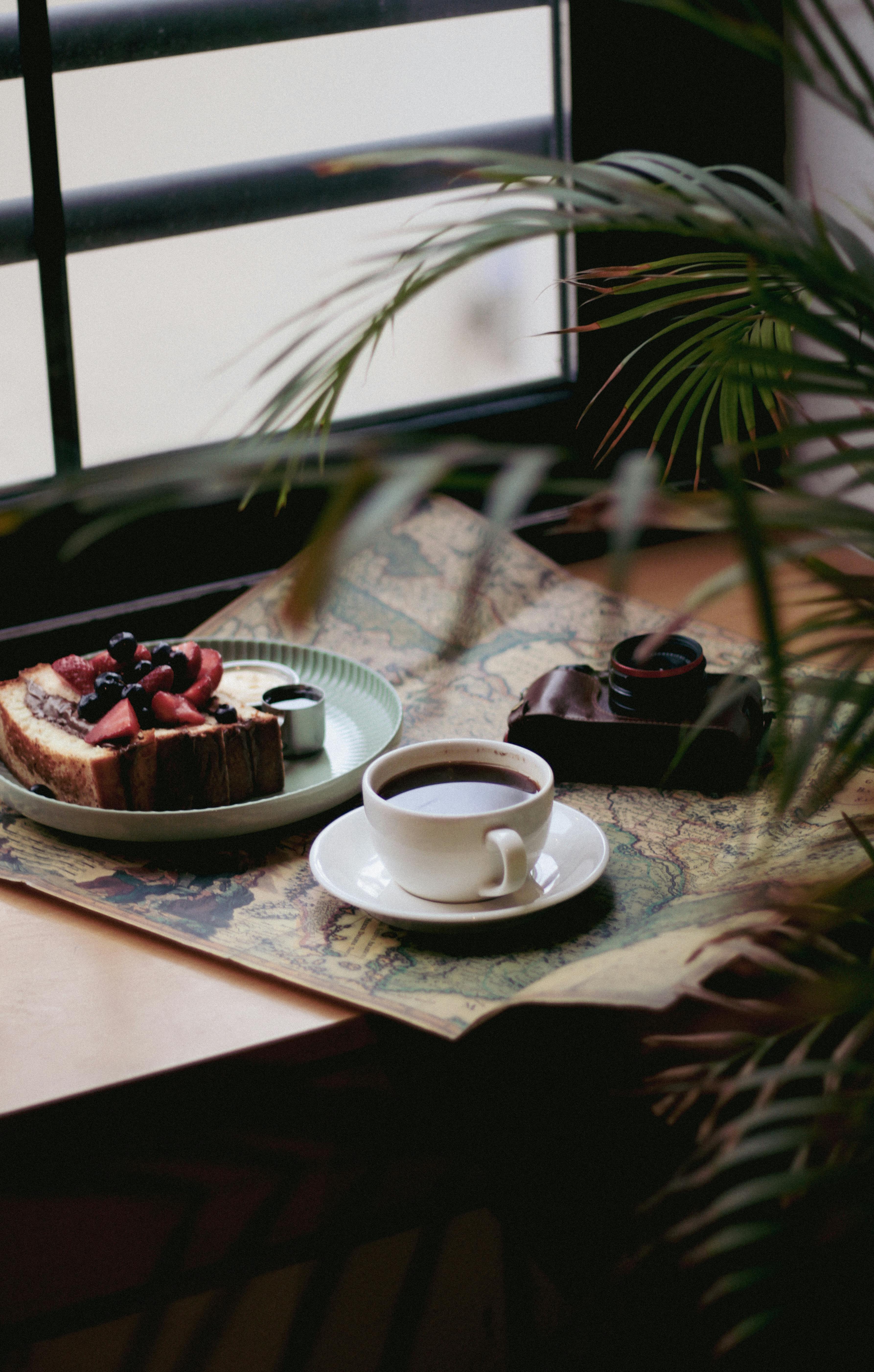 Cup of coffee and desserts on a table by a window, providing a warm and inviting café atmosphere.