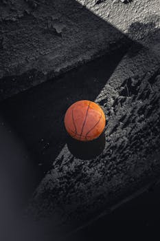 A lone basketball casting a shadow on a rough textured surface, creating a dramatic visual effect.