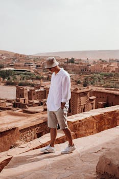 Man strolling through the ancient city of Aït Benhaddou, Morocco, wearing casual attire with a sun hat.