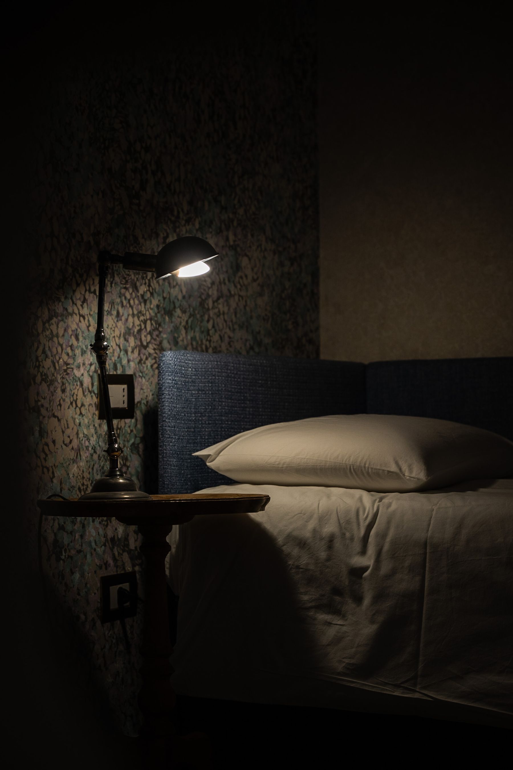 Warm desk lamp illuminating one pillow and part of a bed while the rest of the room remains dark