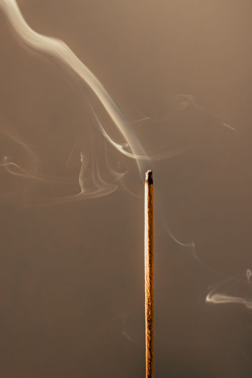 Free A tranquil close-up of a burning incense stick emitting delicate smoke against a neutral background. Stock Photo