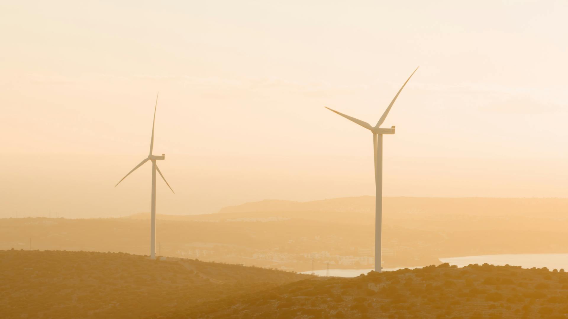 A serene sunset view of wind turbines in the rural hills of Çeşme, Türkiye, depicting renewable energy in harmony with nature.