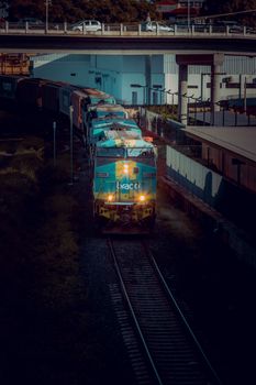 Dark mood captures a freight train approaching an urban railway station at twilight.
