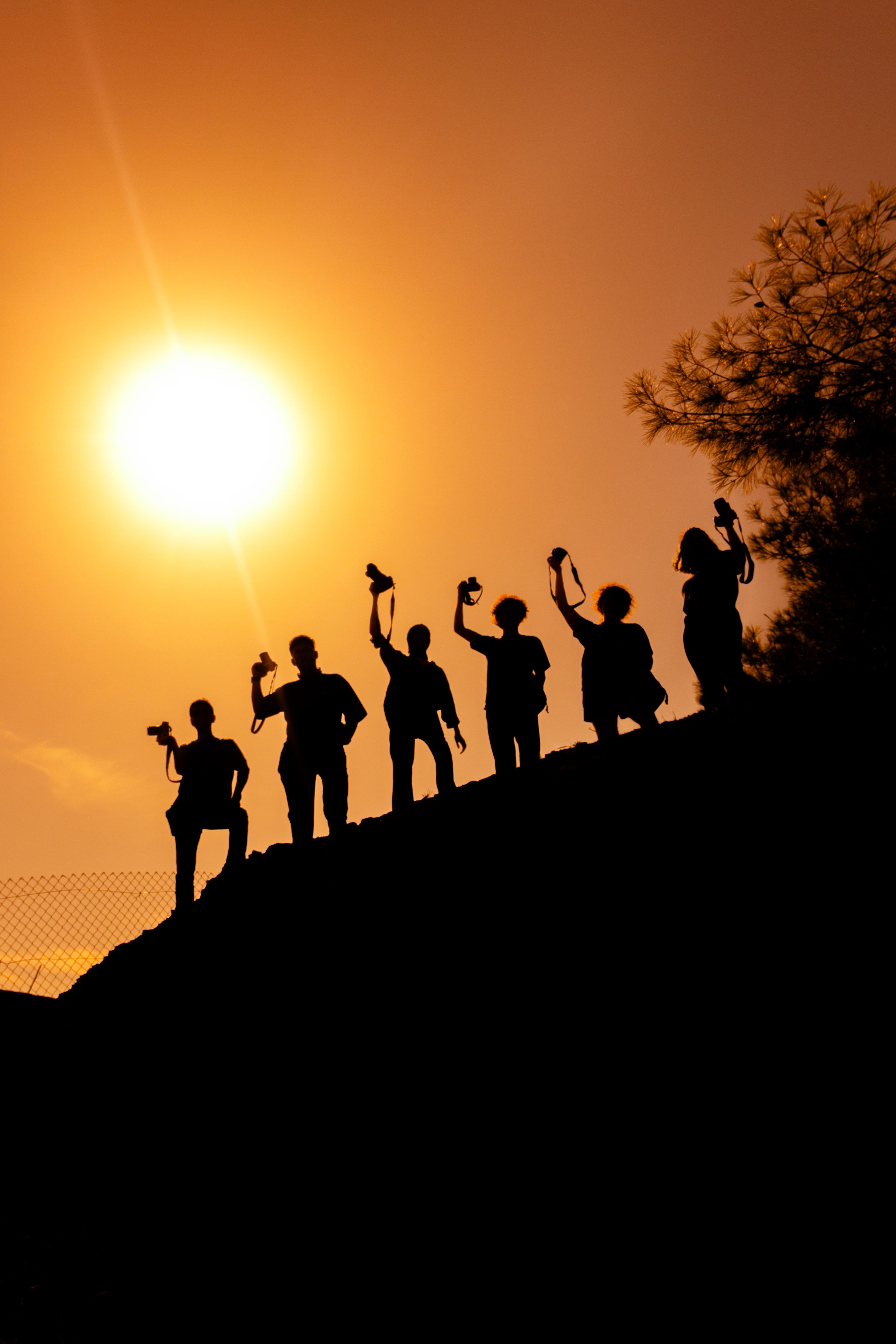 Silhouetted photographers holding cameras against a vibrant sunset on a hill.