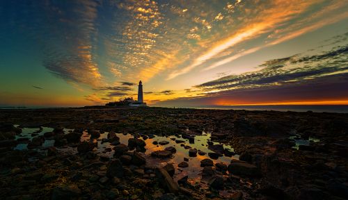 Free Dramatic sunset view of St Mary Lighthouse on Northumberland coast, reflecting in tidal pools. Stock Photo