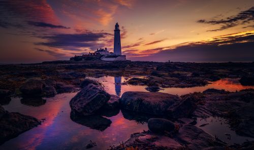 Free Serene sunset view of a lighthouse reflecting in tidal pools, creating a picturesque silhouette. Stock Photo