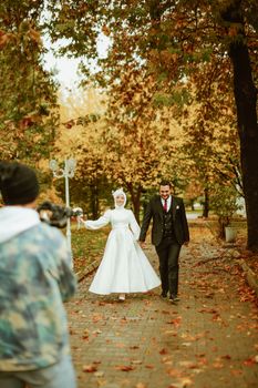 Captivating autumn wedding captured in urban park with bride in hijab and groom in suit, walking joyfully.
