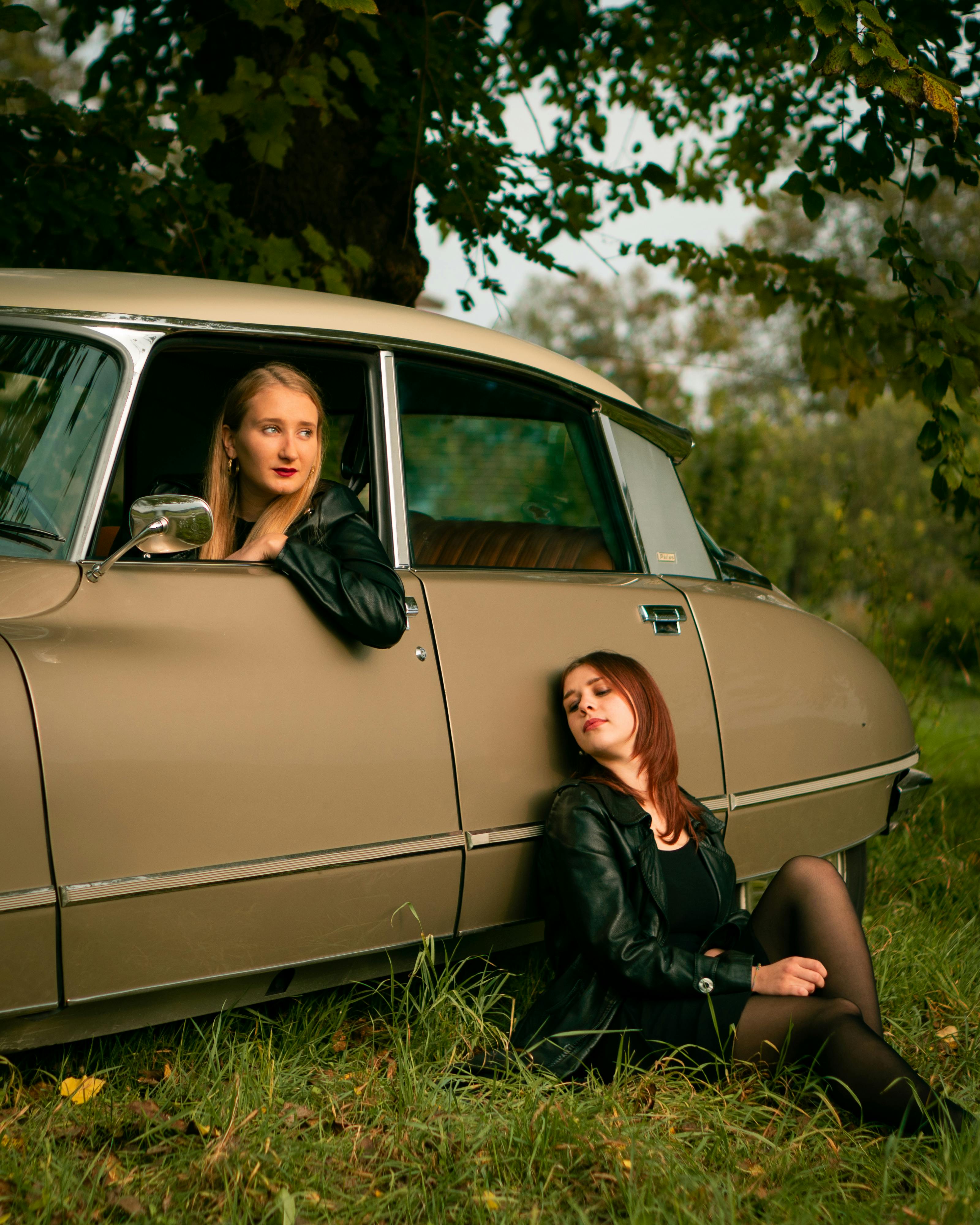两名身穿皮夹克的女子站在树下的老爷车旁，营造出经典而怀旧的感觉