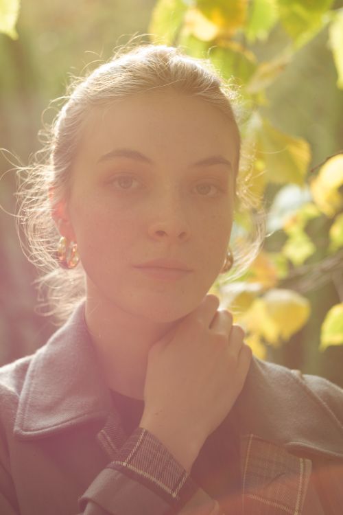 Free A serene portrait of a woman bathed in gentle sunlight amidst autumn leaves. Stock Photo