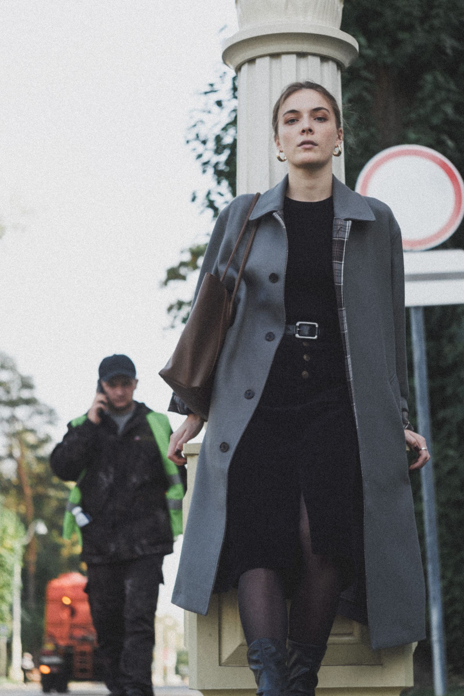 Model in a long grey coat and black dress walking on a city street.