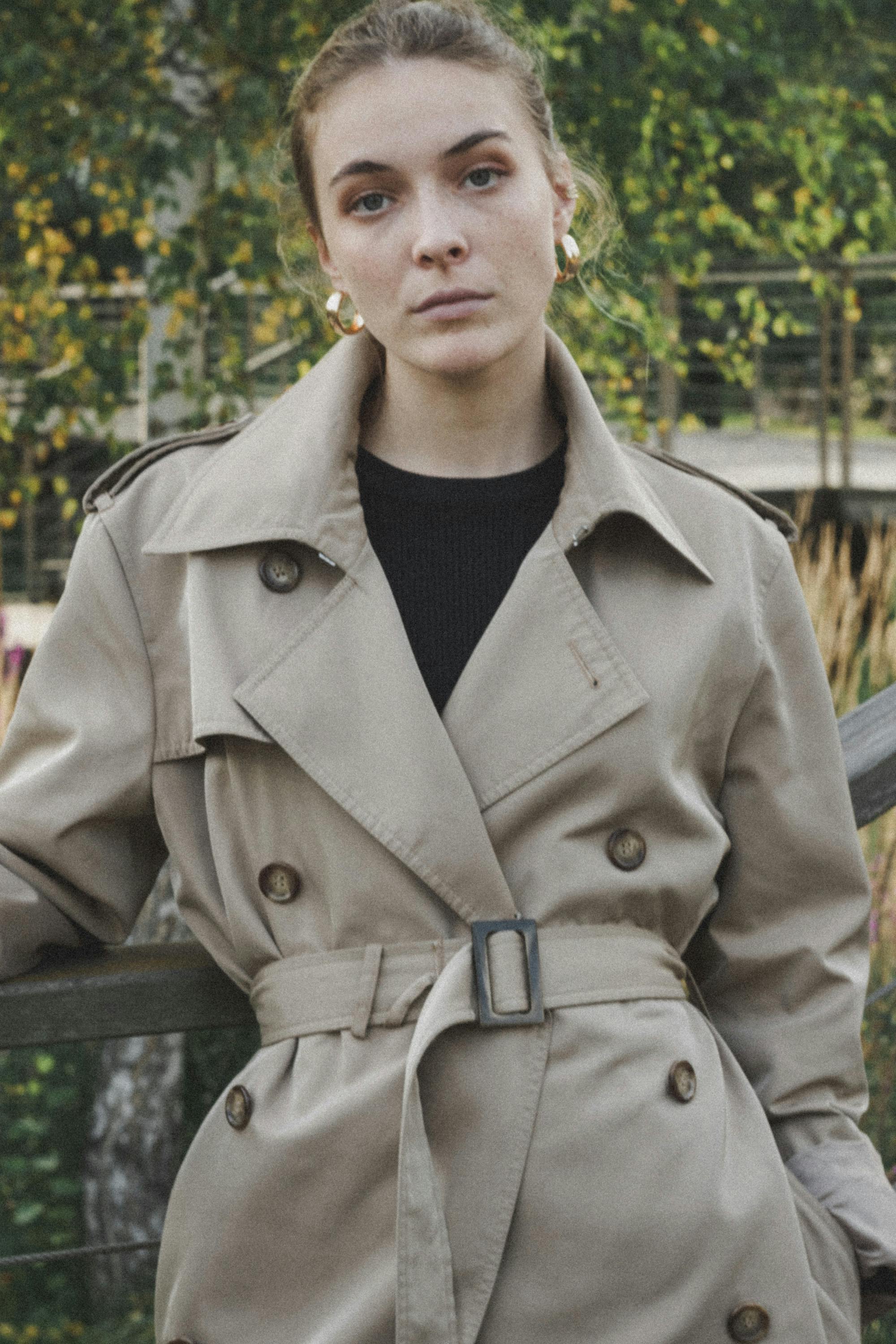 Brunette woman wearing a trench coat posing outdoors in autumn.