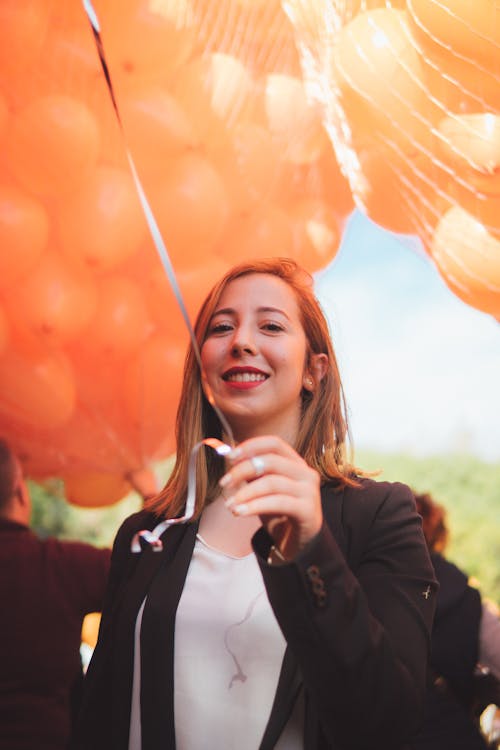 Photo of Smiling Woman Holding Bundle of Orange Balloons