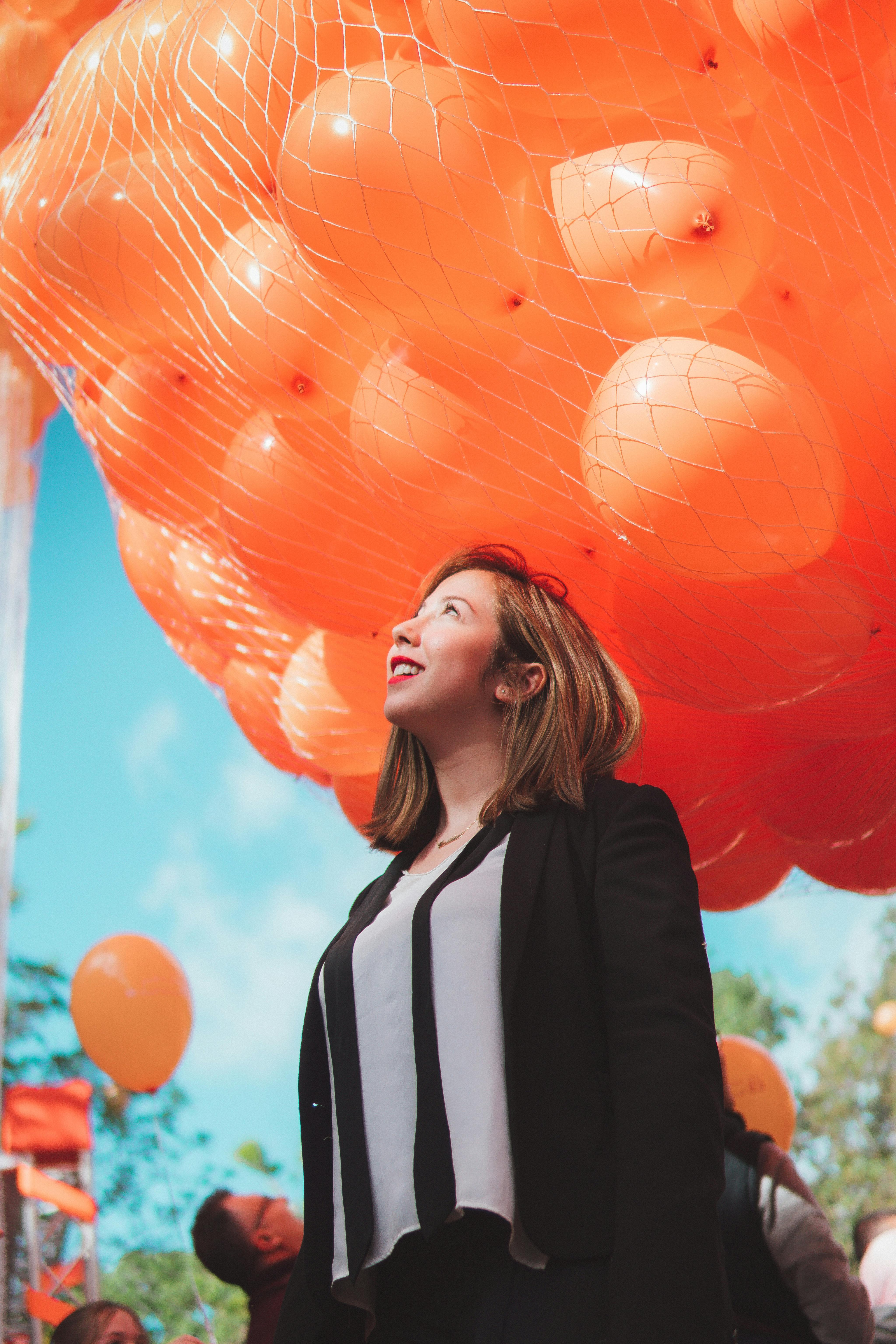 woman in black cardigan smiling under orange balloons