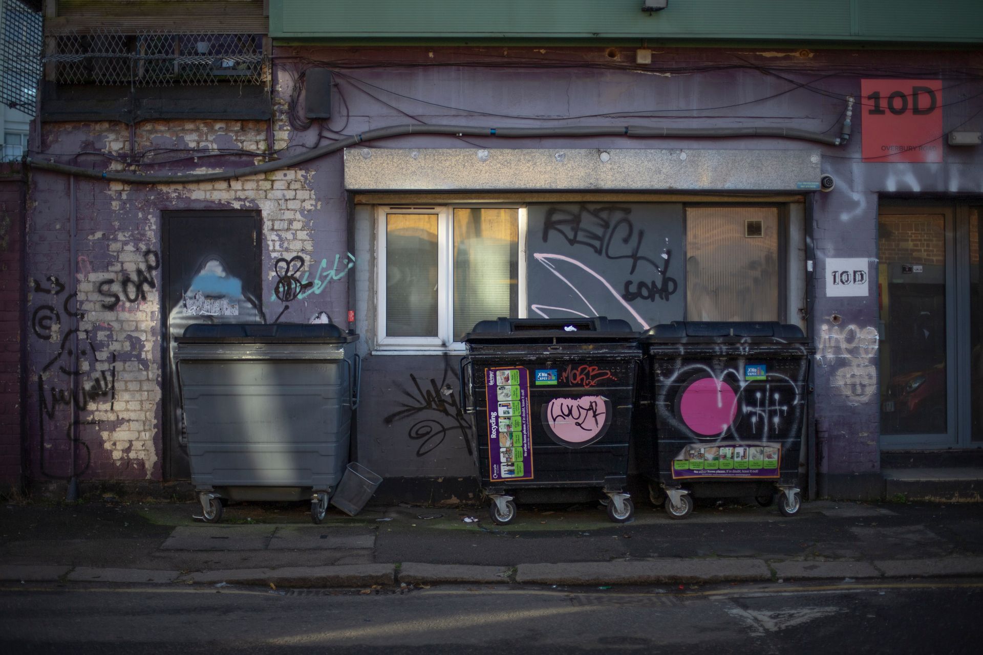 Graffiti-covered alley in London featuring garbage bins and urban architecture.