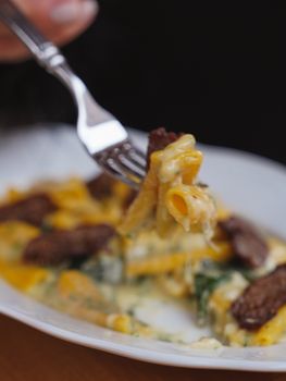 Close-up of creamy pasta with grilled steak on a fork, showcasing delicious textures.