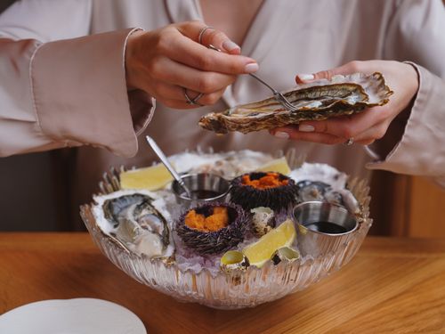 Free Close-up of a person enjoying fresh oysters and sea urchins in a fine dining setting, showcasing luxurious seafood cuisine. Stock Photo