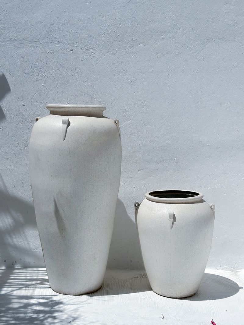Two matte white vessels against a bare plaster wall — photo by Wolf Art on Pexels
