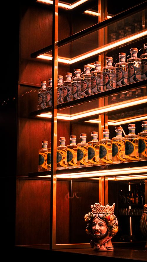 Free Stylish display of bottles on backlit shelves with artistic bust in modern bar setting. Stock Photo