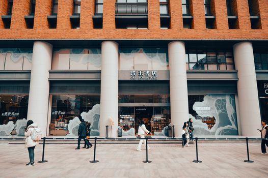 People walking by a modern bookstore with columns in a city setting.