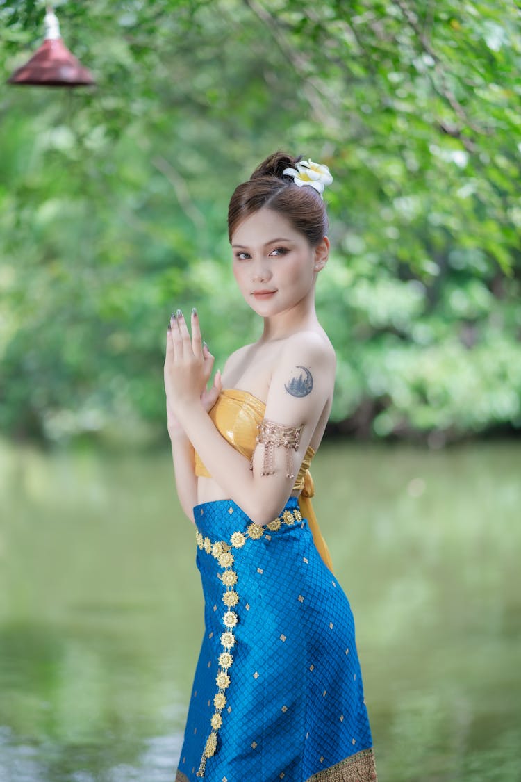 Model In A Tie Back Golden Tube Top And A Blue Printed Skirt With Folded Hands By The River