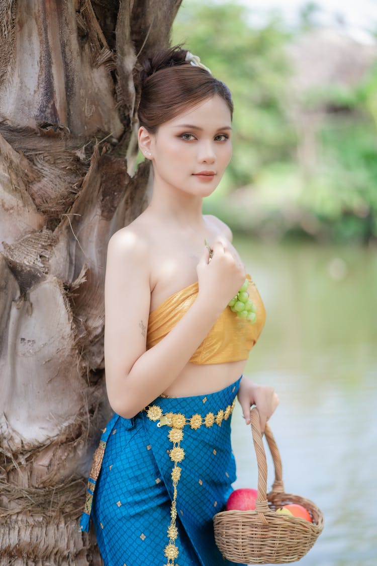 Model In A Golden Tube Top And A Blue Printed Skirt Holding A Basket Of Fruits