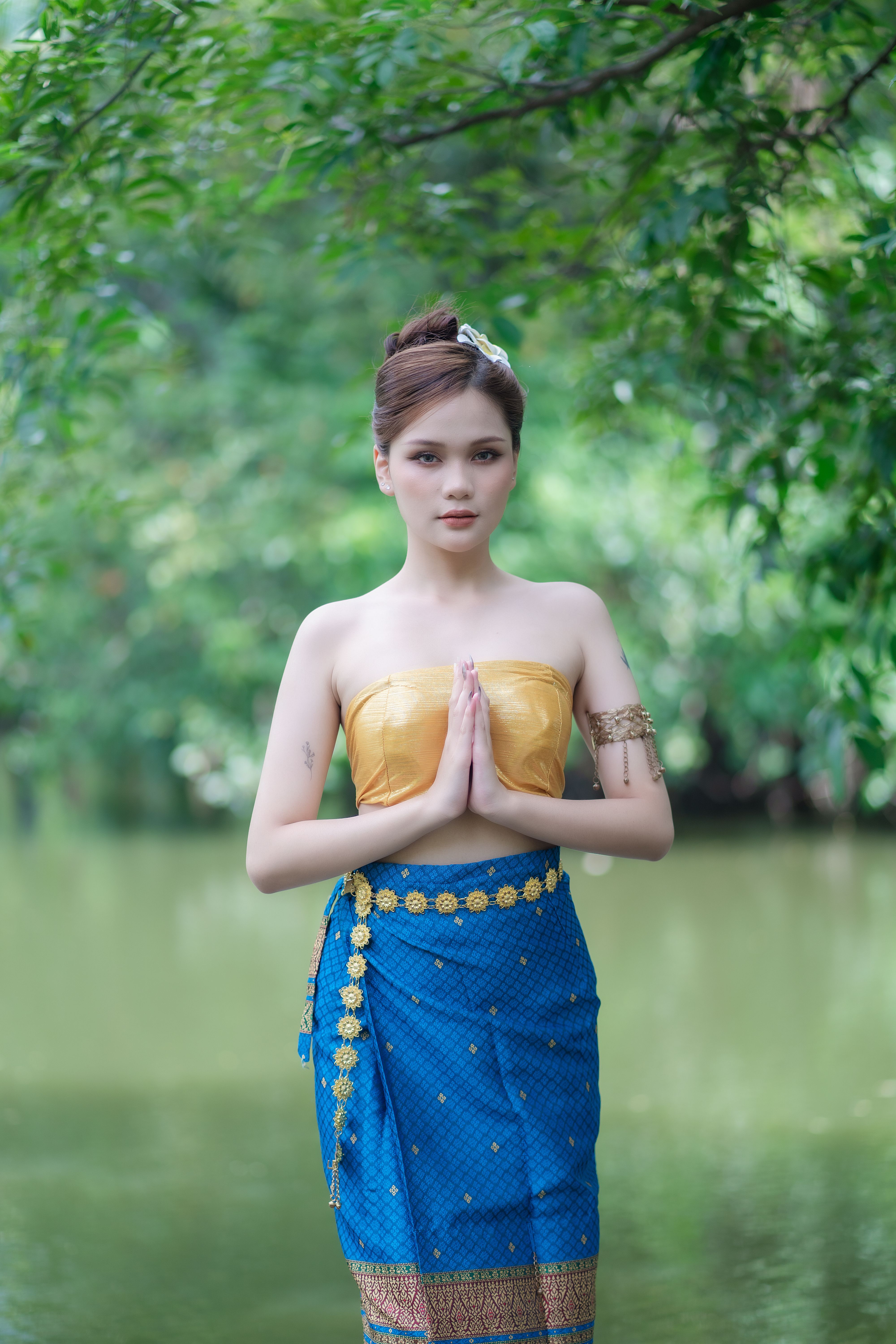 A young woman poses gracefully in traditional Thai clothing by a serene river