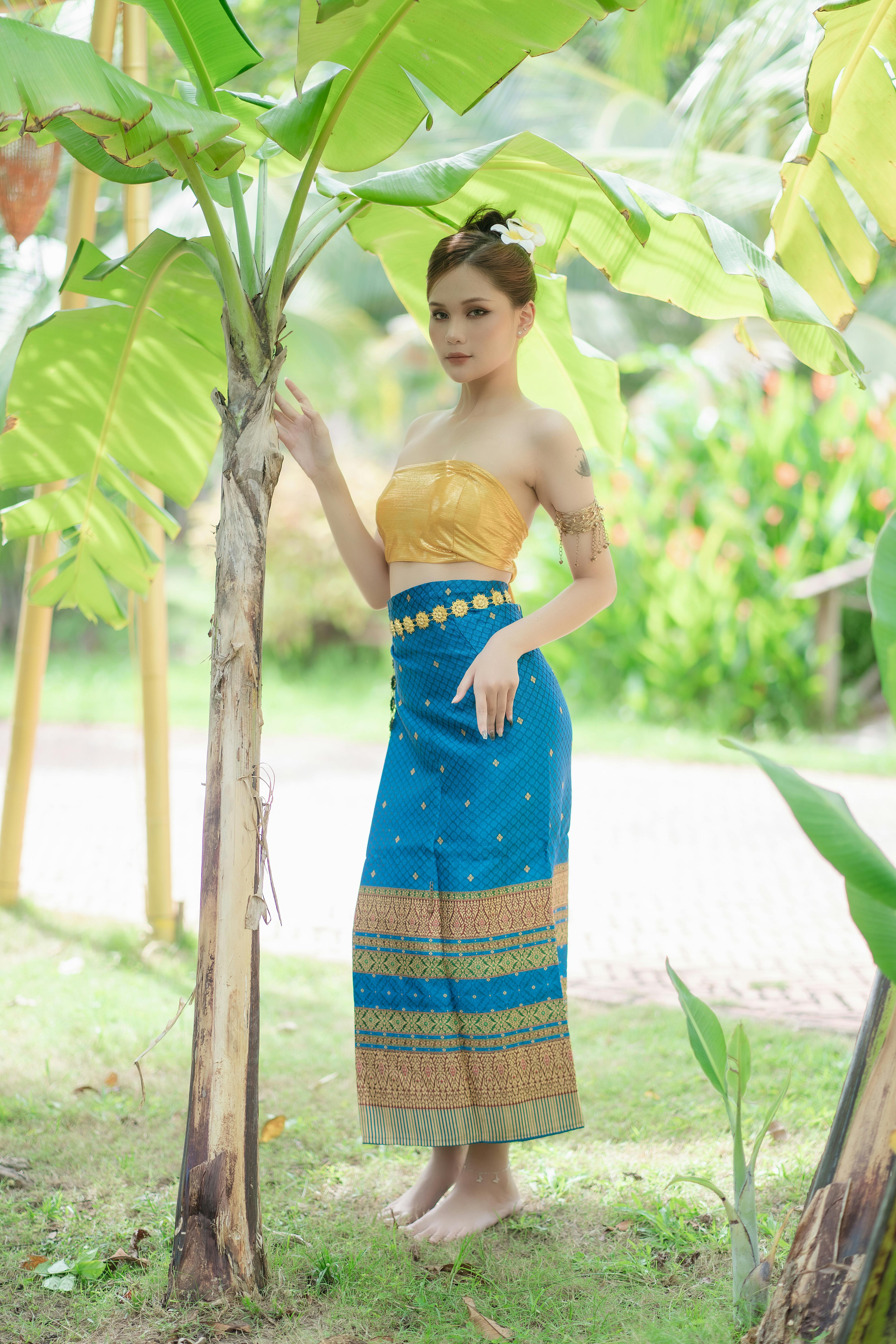 model in a golden tube top and a blue printed skirt in the park under the tree