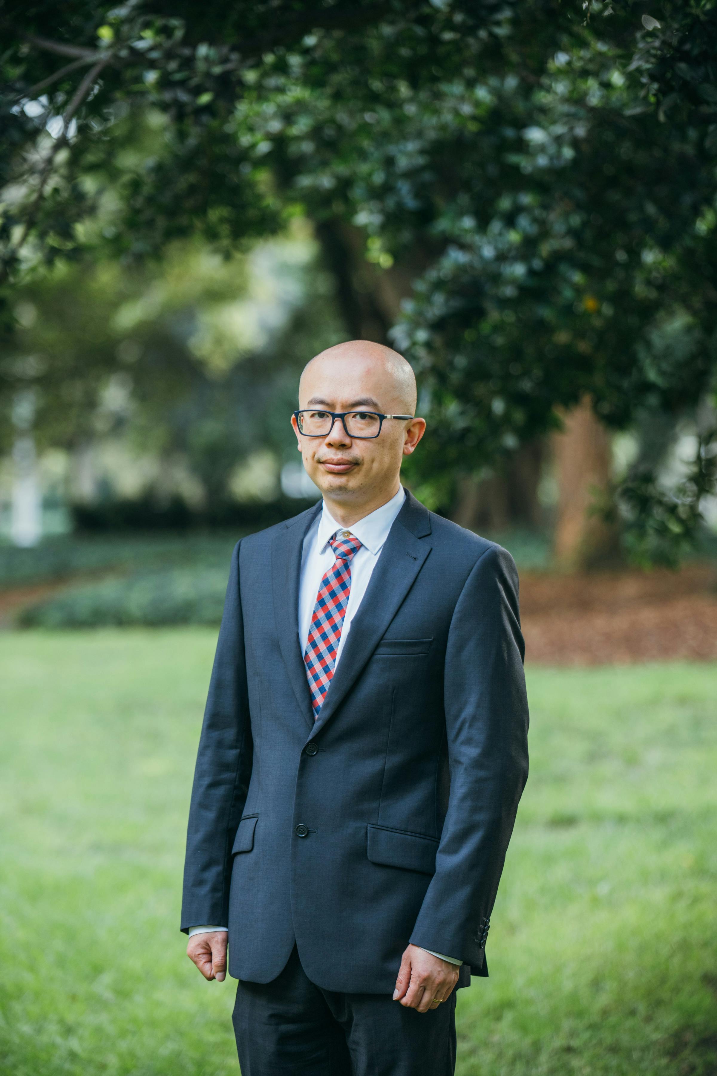 Elegant portrait of a bald Asian businessman in suit with eyeglasses standing outdoors in Sydney.