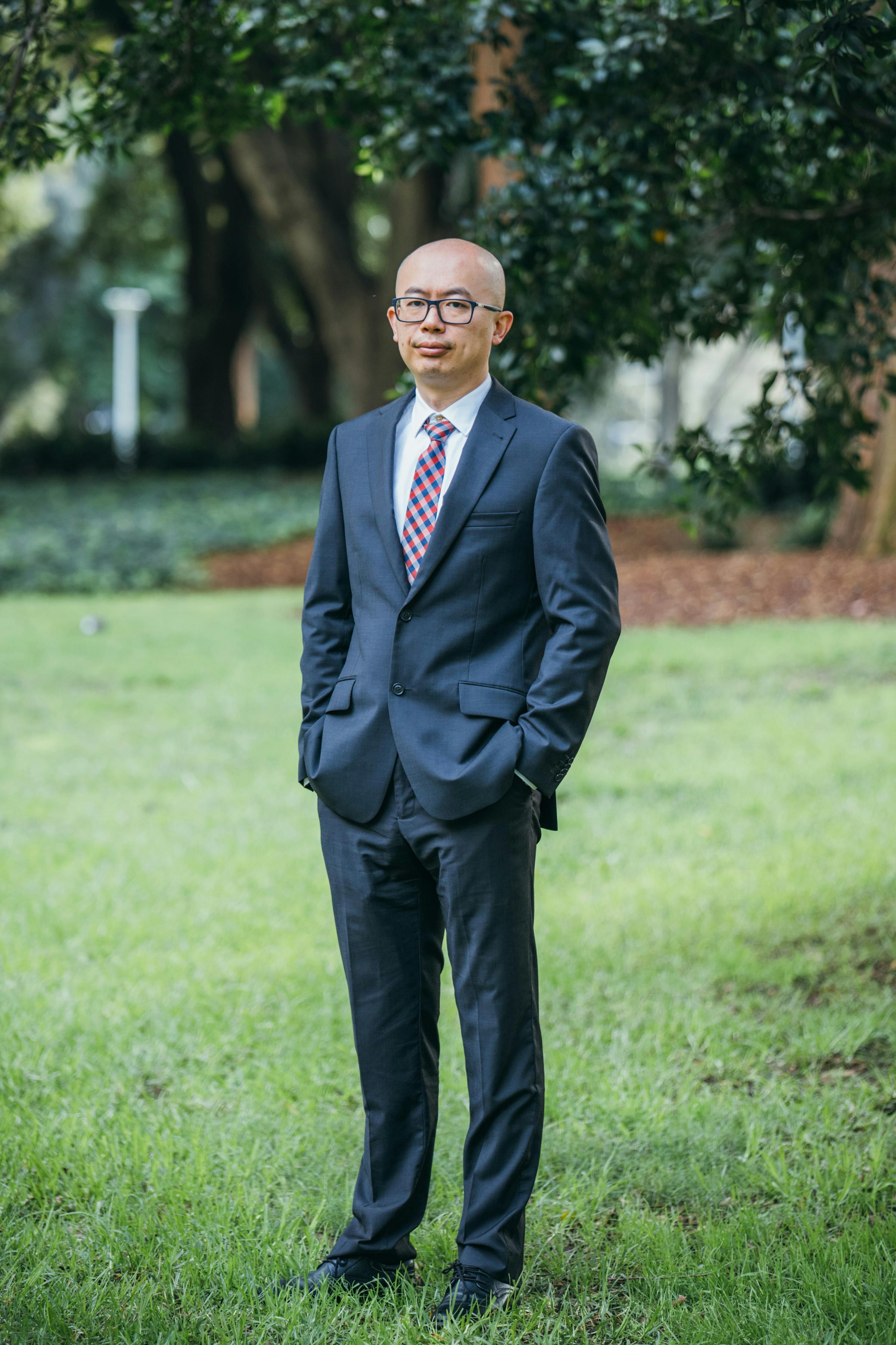 Asian businessman in a suit standing gracefully in Sydney park outdoor setting.