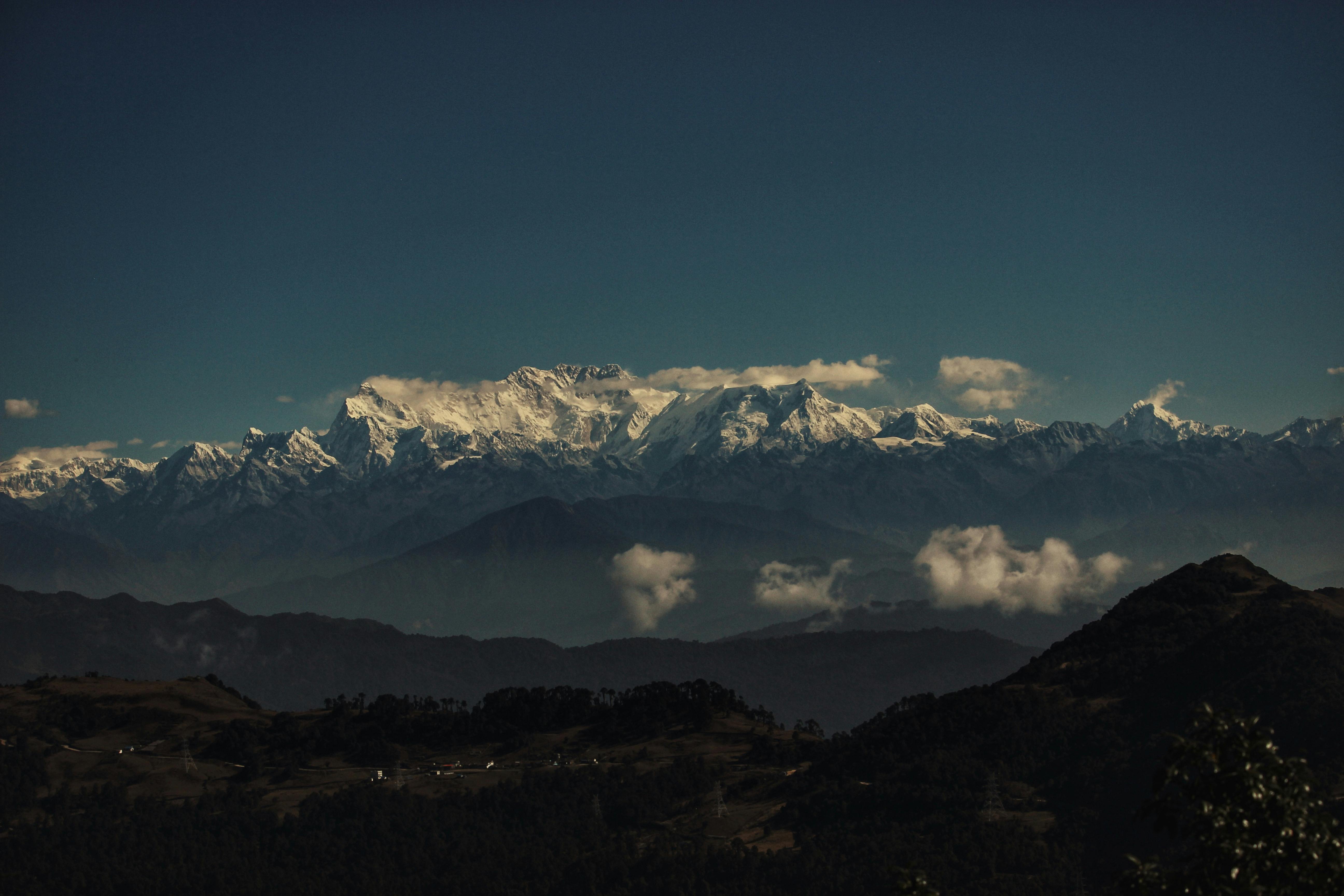 Breathtaking view of the snow-capped Himalayas with clouds and hills at twilight.
