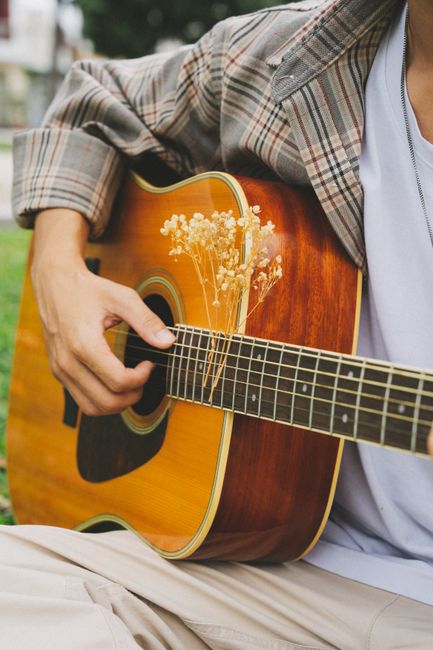 A musician in a plaid jacket plays an acoustic guitar with skill outdoors.