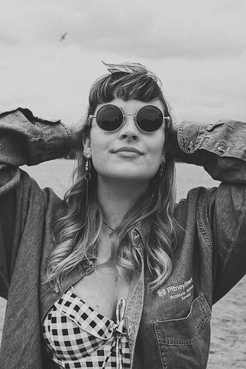 Free Black and white portrait of a smiling woman in sunglasses wearing a jean jacket by the sea. Stock Photo