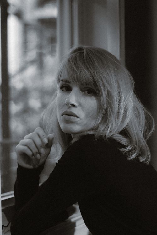 Free Elegant black and white portrait of a woman with blonde hair looking out a window. Stock Photo