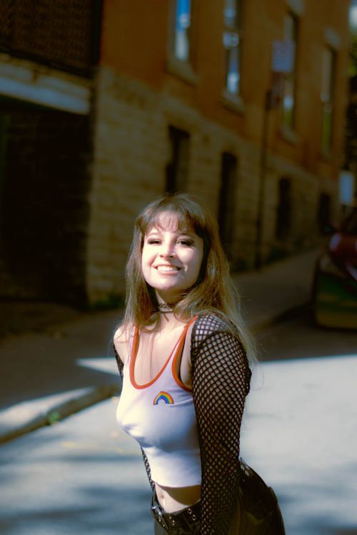 Free A smiling young woman enjoying a sunny day on a city street, wearing a fashionable white top. Stock Photo