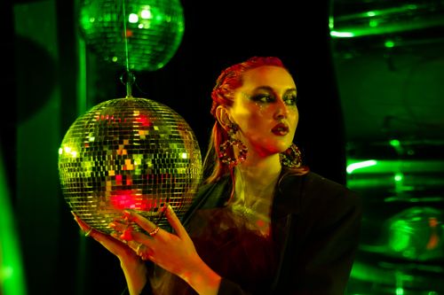 Free A stylish woman wearing large earrings and holding a disco ball, creating a vibrant party atmosphere. Stock Photo