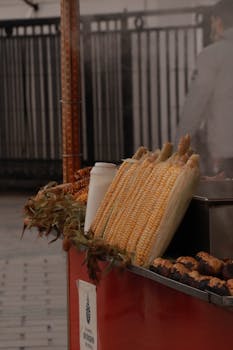 Fresh corn cobs displayed on a street food vendor's grill cart outdoors.