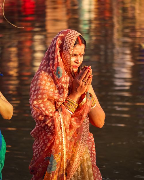 Free A woman in traditional clothing stands with hands clasped in prayer by the water. Stock Photo