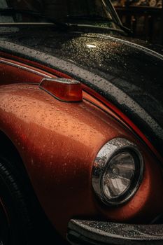 Close-up of a vintage car's headlight and raindrops at night, showcasing classic design.