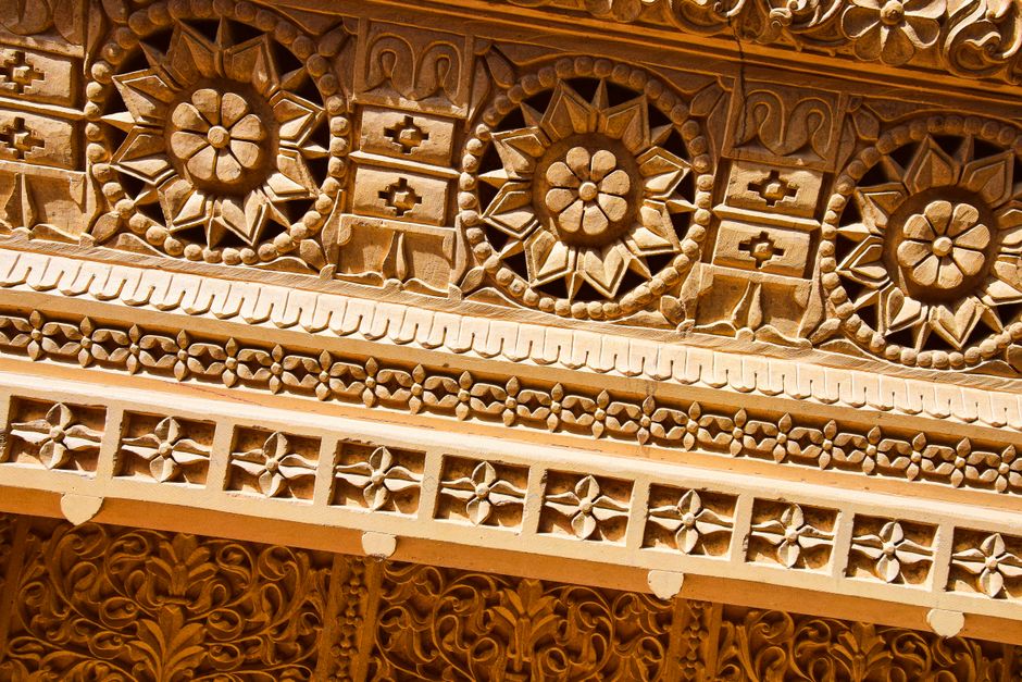 Detailed close-up of sunlit ornamental carvings on Indian sandstone wall.
