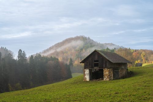 Free A serene countryside scene featuring a rustic barn in a misty, autumn landscape. Stock Photo