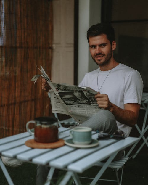Smiling Man with Newspaper Sitting by Table
