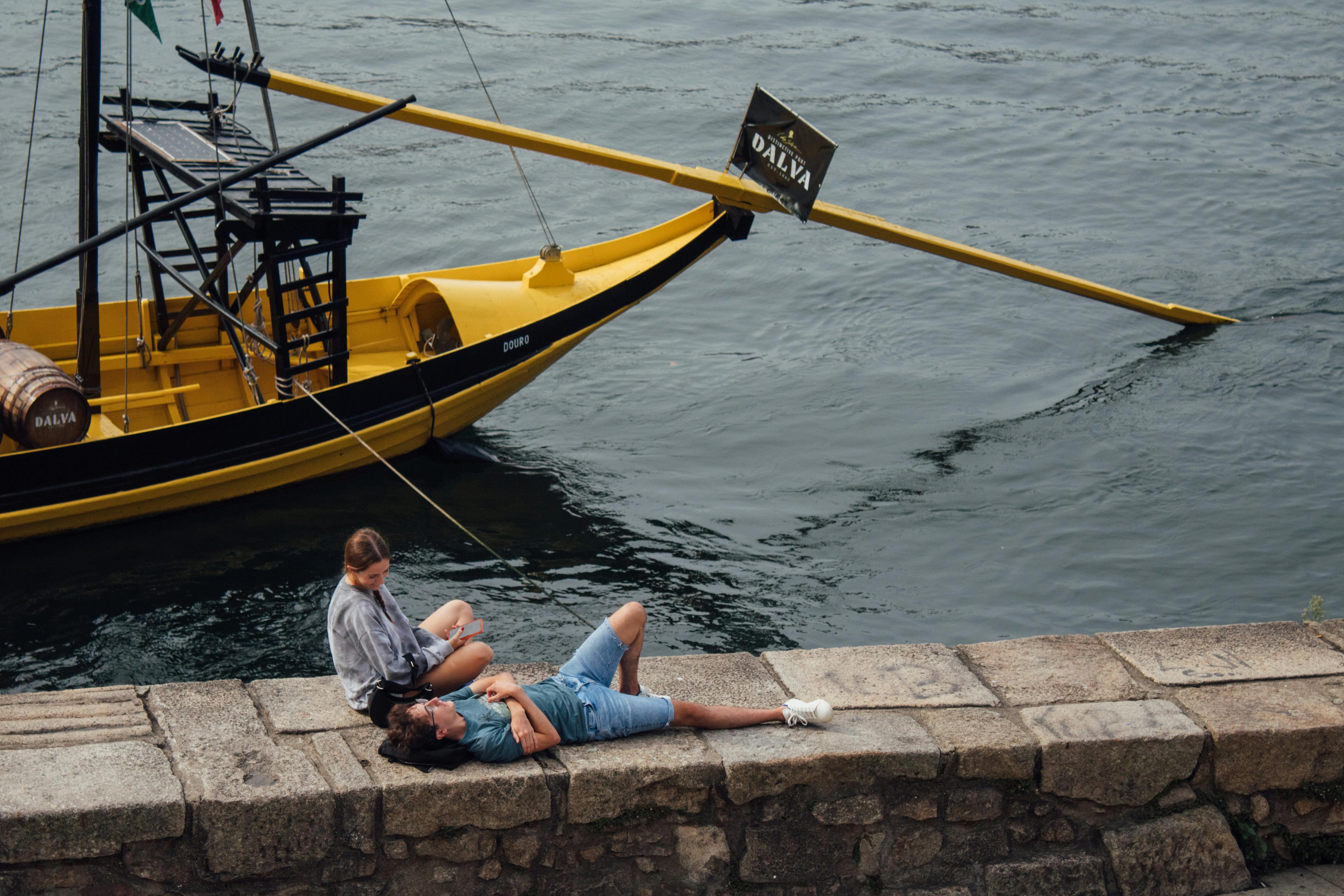 Couple enjoying a peaceful moment by the Douro River in Porto, Portugal, with a traditional rabelo boat nearby.