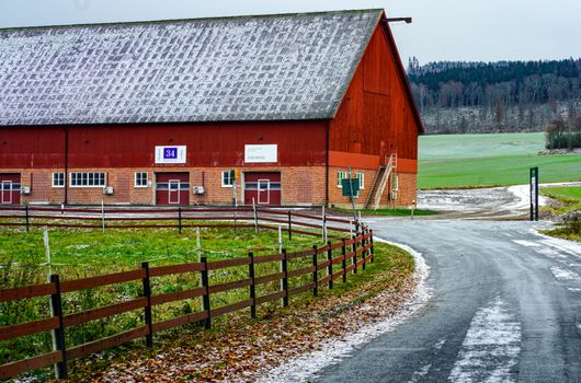 A picturesque red barn by a snowy road in a serene rural setting.