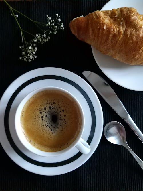 Free Cup of Dark Coffee on a Saucer and a Croissant Stock Photo