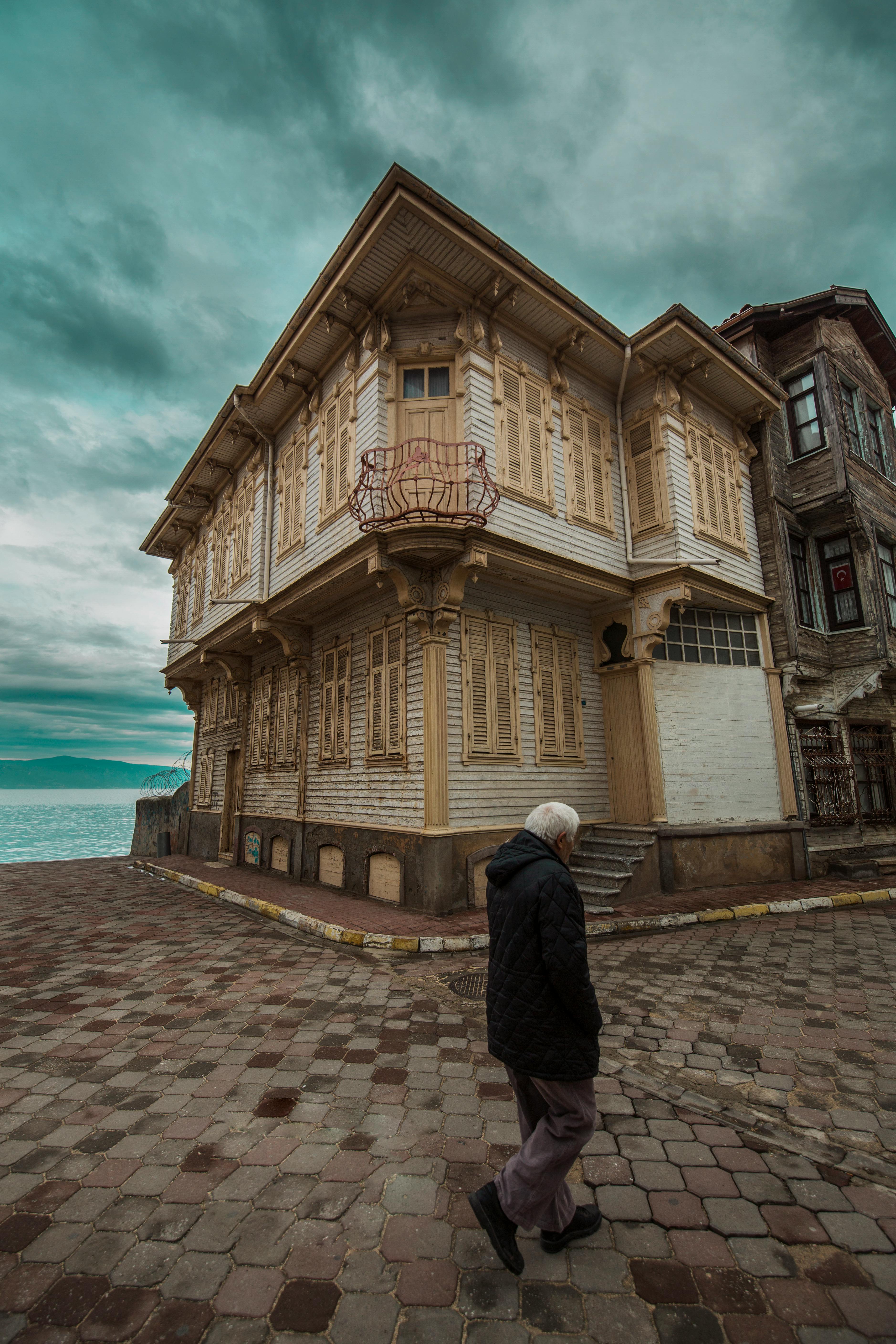 Free Elderly man walking by a classic wooden house on a cloudy day by the sea. Stock Photo