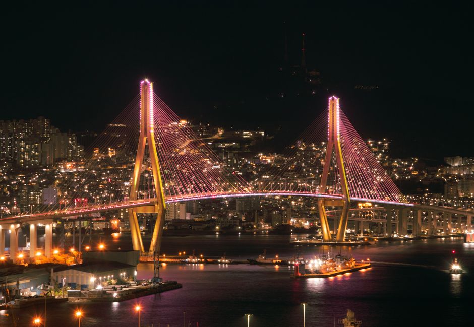 Stunning nighttime view of the illuminated Busan Harbor Bridge in South Korea, highlighting the city's vibrant skyline.