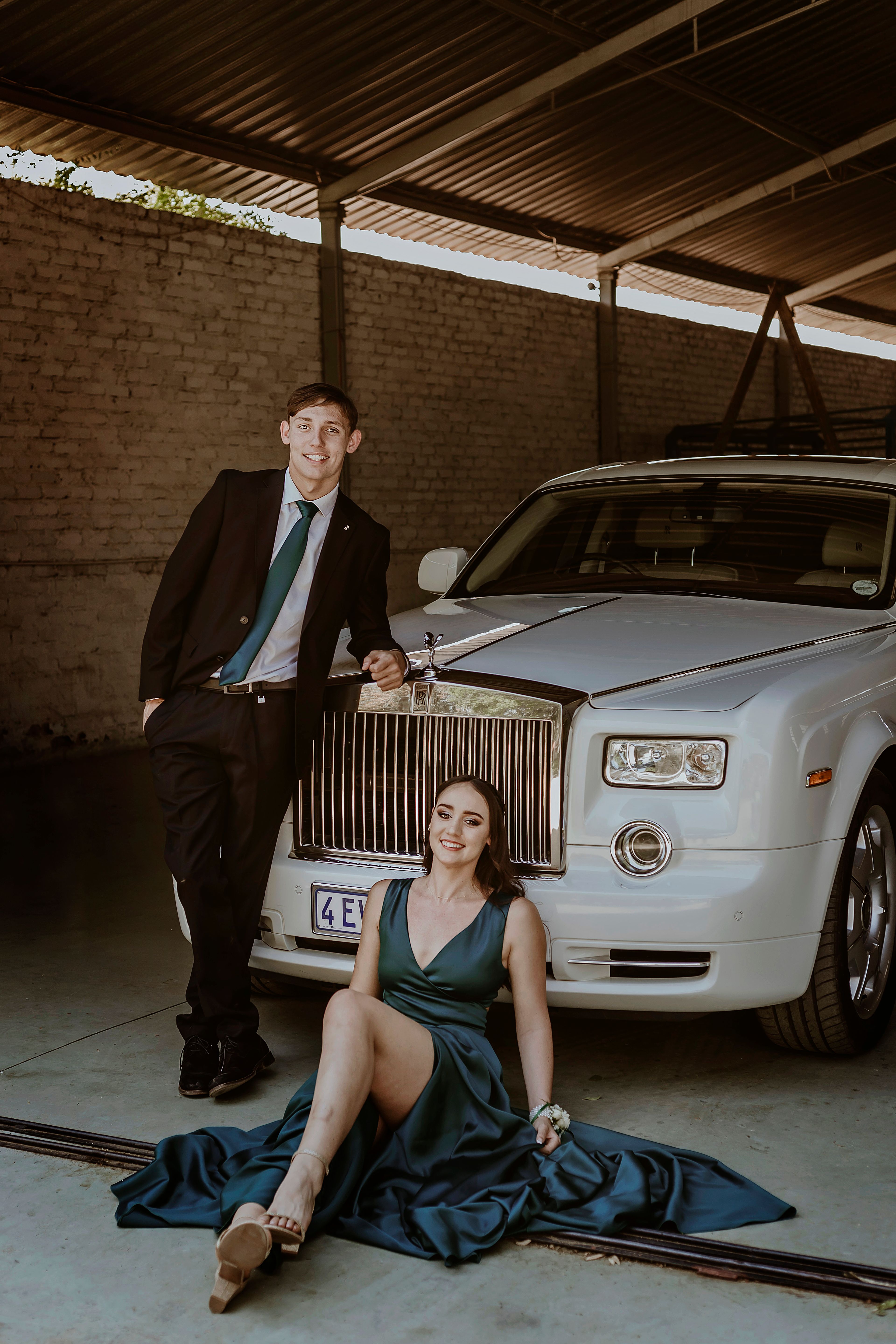 Chic couple exuding sophistication beside an opulent car indoors.