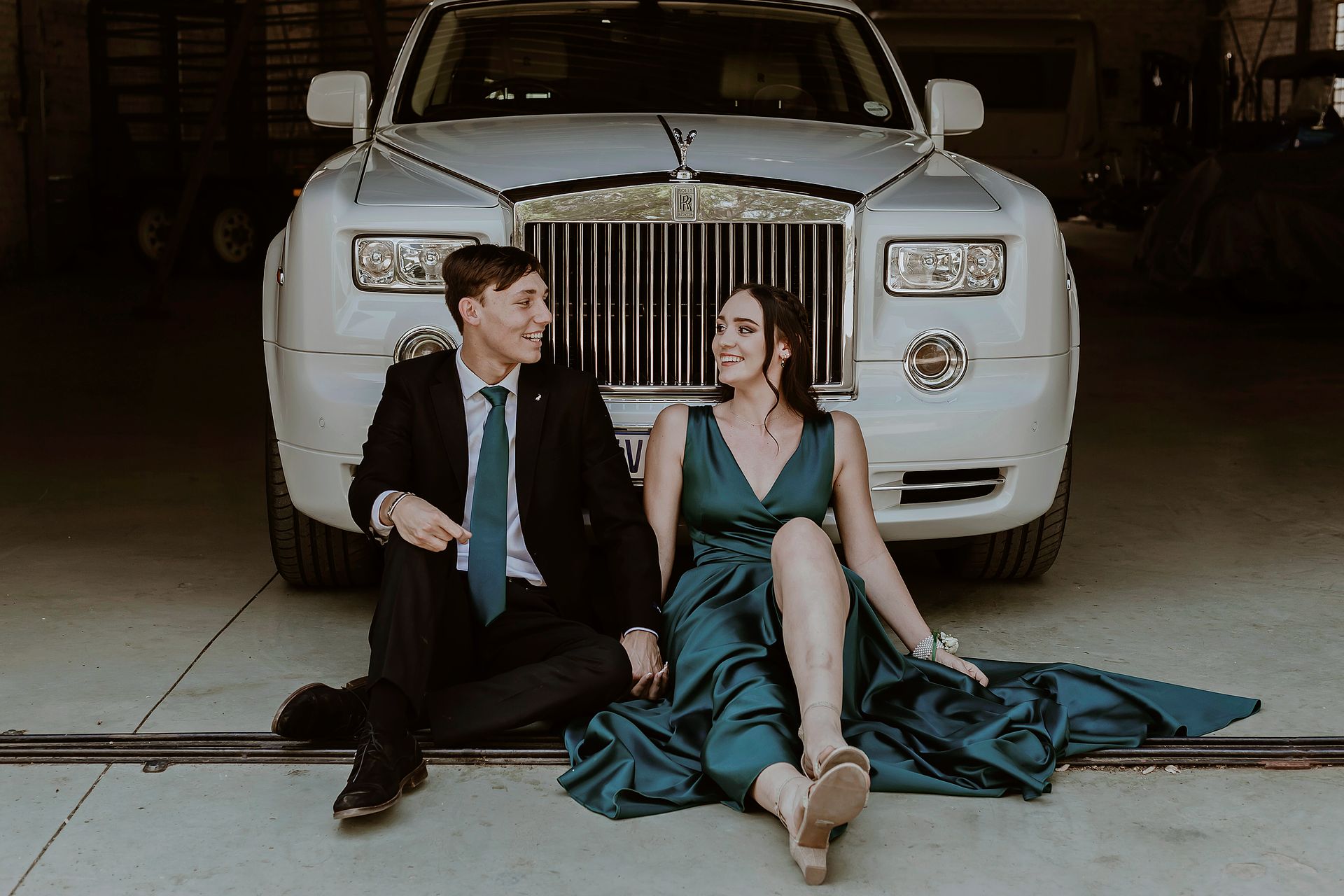 A stylish couple in formal attire poses by a luxury car, exuding elegance in Pretoria, South Africa.