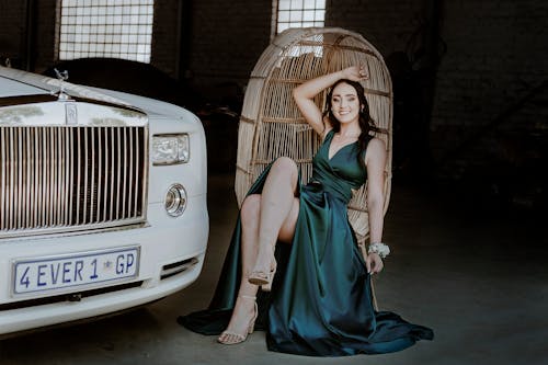 Young Woman Sitting on a Wicker Chair by a Luxury Car 